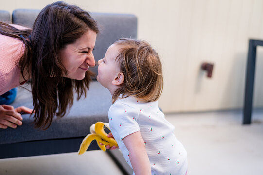 Italian mum leaning forward meeting toddler daughter at eye level to touch each others noses
