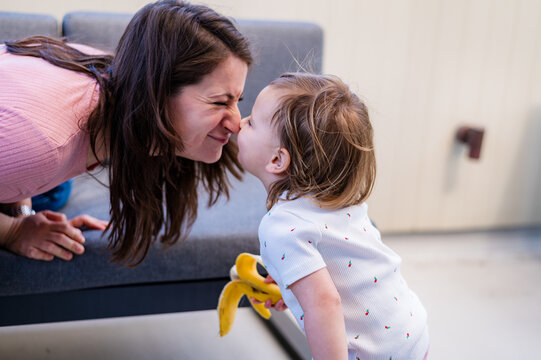 Italian mum leaning forward meeting toddler daughter at eye level to touch each others noses
