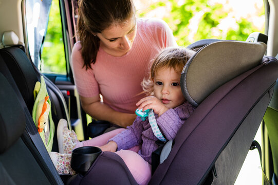 Woman in pink shirt securing child in rear-facing car seat inside vehicle