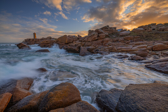 View of Ploumanac'h Lighthouse and pink granite rocks with crashing waves under a sunset sky in Perros-Guirec, Bretagne, France.