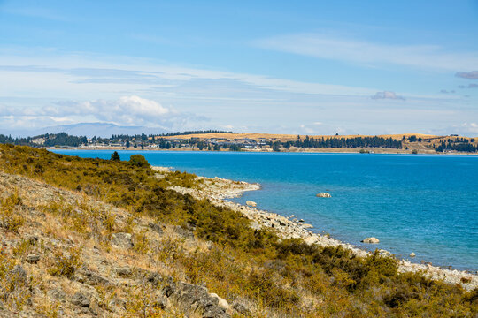 View across blue lake from grassy slope with a rocky shoreline