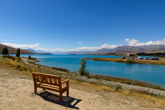 Wooden bench seat overlooking a blue lake with church and mountains in background