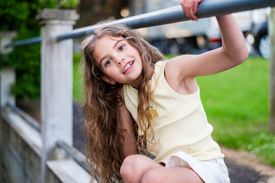 Young girl with long hair holding on a metal railing outside home near paved path