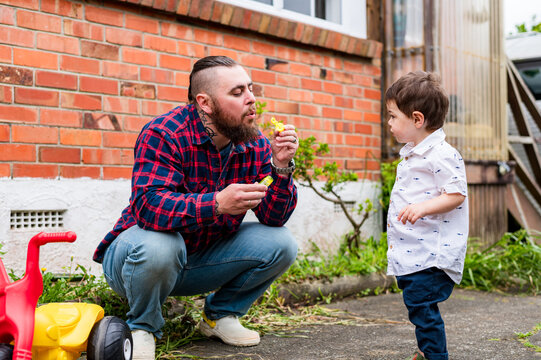 Dad crouching on the paved ground in the backyard playing bubbles with toddler son outdoors
