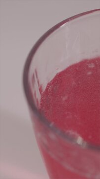 Vertical close-up focusing on the effervescent process. Red bubbles and fizzing texture inside the glass, symbolizing energy and health recovery.