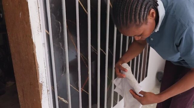 Black gate house chores, cleaner wiping bars with towel and cloth, close handson motion removing paint chips and stains, blue shirt sleeve, steady domestic routine, concentrated effort