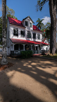 View of a historic colonial wooden house with a red roof and green shutters under a clear blue sky in Paramaribo, Paramaribo District, Suriname.