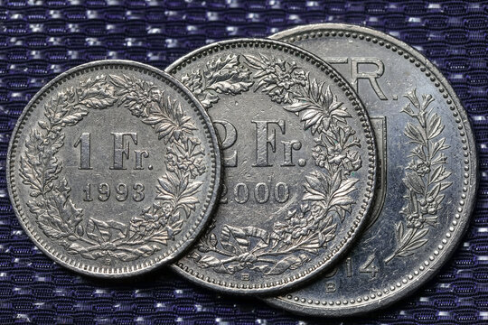 Three different Swiss coins are visible against a dark fabric background