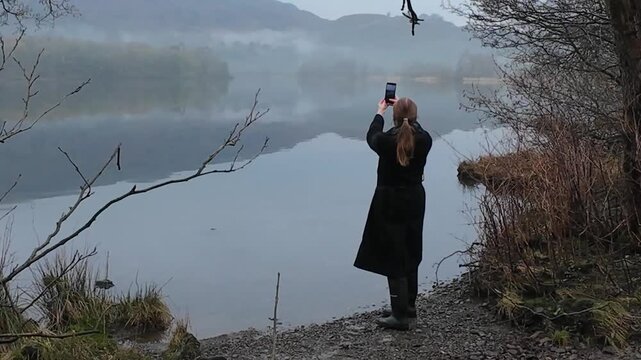 Woman taking photo of a lake in winter Lake District