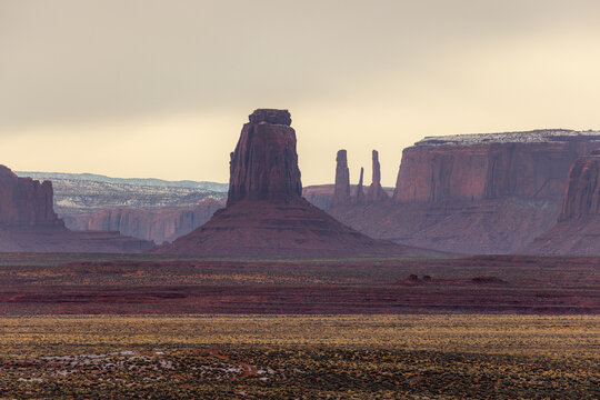 View of the iconic red sandstone buttes and desert landscape under an overcast sky in Oljato-Monument Valley, Arizona, United States.