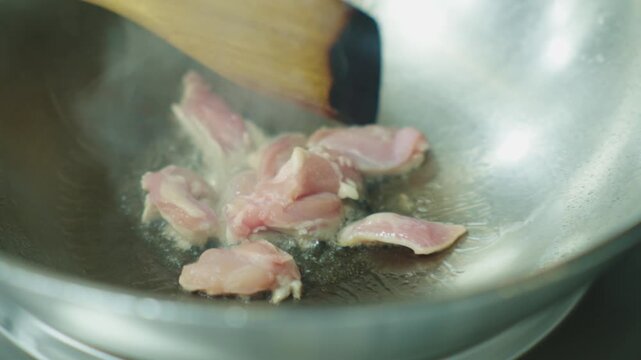 A chef fries chicken meat in a deep iron wok. Asian food in oil.