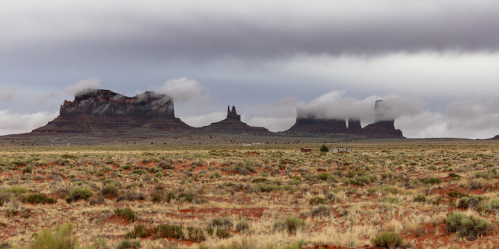 View of the iconic red sandstone buttes of Monument Valley partially shrouded in low clouds under a dramatic overcast sky in Oljato-Monument Valley, Arizona, United States.