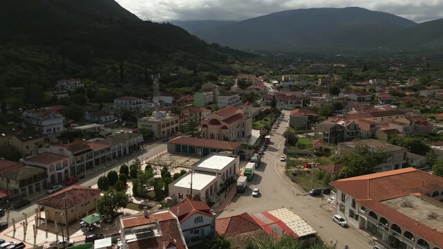 Scenic aerial view of a Mediterranean town nestled at the foot of a lush green mountain under a cloudy sky.