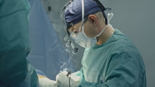 Professional doctor man male surgeon using electrocautery instrument with smoke doing precise neurosurgical procedure operating physician practitioner with assistant intern two men surgery medicine