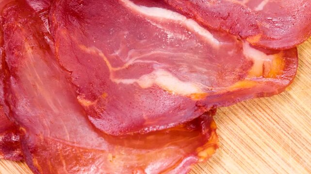 Slices of cured spanish loin lomo embuchado rotating on wooden cutting board showing marble texture