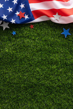 Draped vertical American flag and glitter stars rest on green grass, ideal background for Fourth of July, Memorial Day, Labor Day and Veterans Day holiday designs