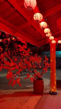A close up nighttime shot featuring festive red lanterns and a decorative peach blossom tree with twinkling lights at Titi Village bus stop in Negeri Sembilan Malaysia.