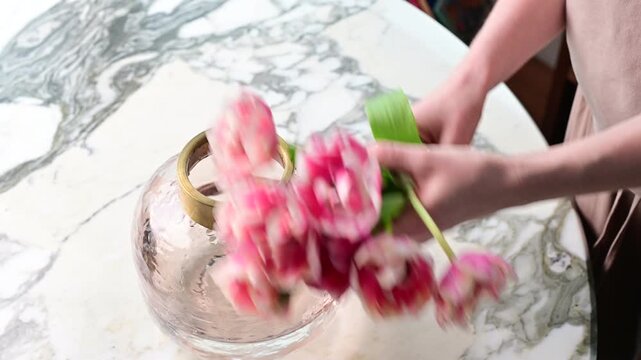 Arranging flowers in a glass vase on a marble table at home in the afternoon light