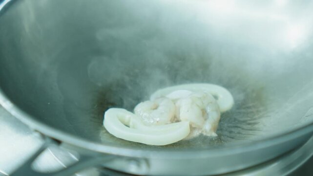 A chef fries seafood with vegetables in a wok. Squid and octopus are fried in oil in a deep metal pan. Cooking seafood
