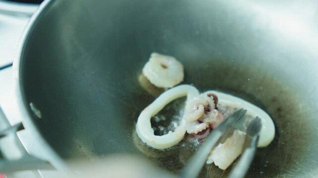 A chef fries seafood with vegetables in a wok. Squid and octopus are fried in oil in a deep metal pan. Cooking seafood