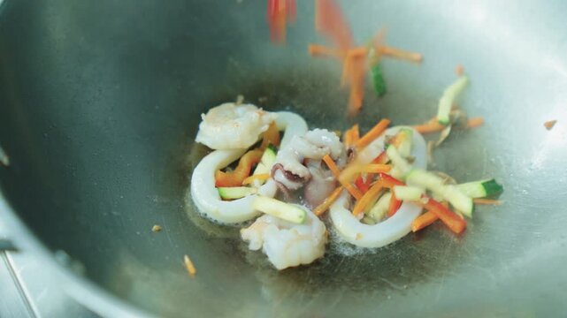 A chef fries seafood with vegetables in a wok. Squid and octopus are fried in oil in a deep metal pan. Cooking seafood