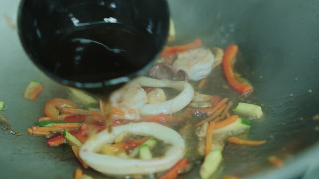 A chef fries seafood with vegetables in a wok. Squid and octopus are fried in oil in a deep metal pan. Cooking seafood