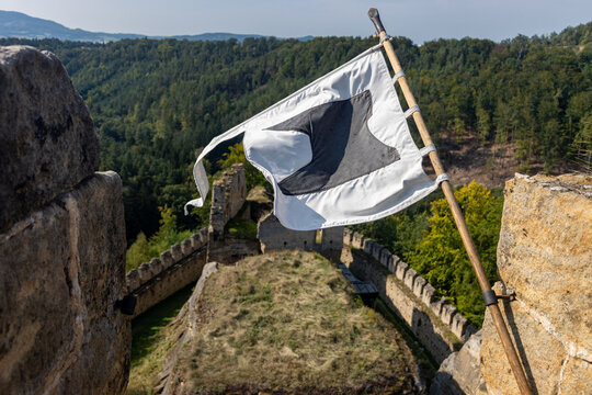 A white flag with a distinctive black emblem hangs on a wooden flagpole attached to a castle tower overlooking at castle