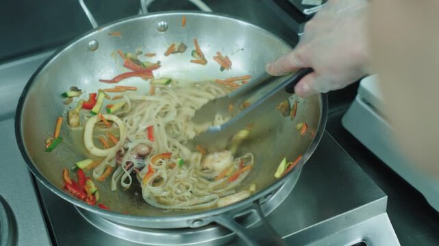 A cook stirs cooked noodles in a wok over a fire. Asian food. Cooking noodles. Stir-frying noodles with vegetables.