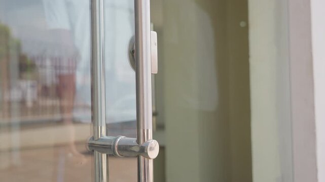 Black technician adjusting glass house door hinge, maintenance worker testing handle alignment and latch, closeup of metal fittings and arm movement, residential facade and reflective window,