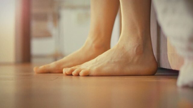 Man slowly rises from bed, his bare feet touching cool floor. He stretches, extending his fingers, as morning sunlight creeps in, signaling start new day, capturing quiet morning concept of waking up