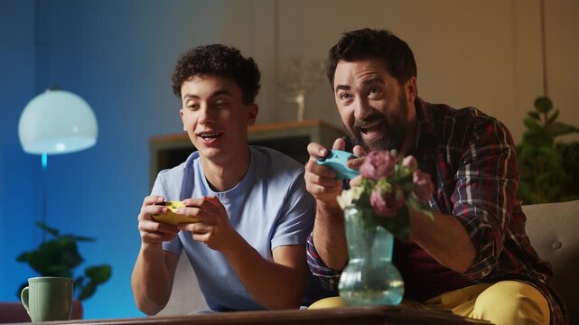Smiling teenage boy and his father playing a video game with joysticks