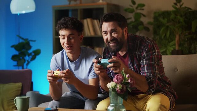Cheerful teen boy and his dad playing a video game with gamepads at home