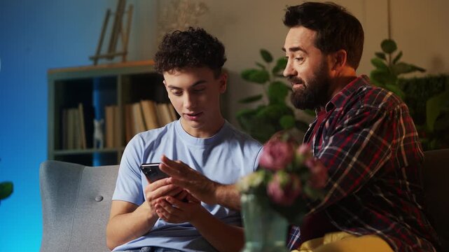 Smiling dad and his teen son discussing a new mobile shopping app on phone