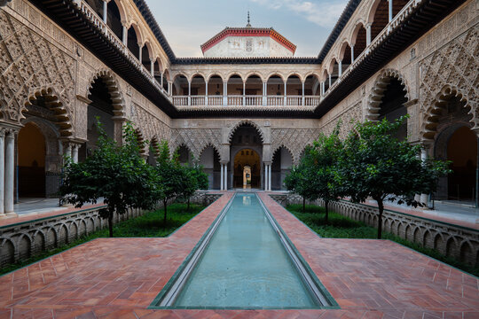 View of the Patio de las Doncellas with its reflecting pool and Mudejar arches in the Royal Alcazar of Seville, Andalusia, Spain.