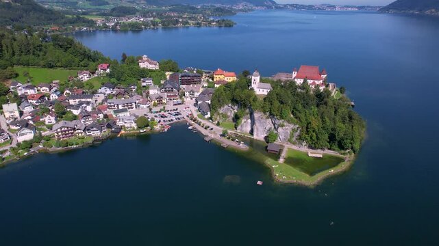 Austria Traunkirchen aerial 4K. Orbit drone video of scenic peninsula with historic monastery and church on Lake Traunsee. Alpine landscape with mountain reflection.  travel scenery