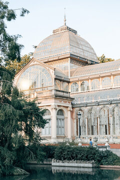 View of the Palacio de Cristal with its glass and iron architecture reflected in the pond and surrounded by lush green trees in Madrid, Community of Madrid, Spain.