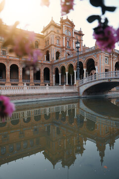 View of the ornate Renaissance Revival architecture of Plaza de Espana with its arched galleries and stone bridge reflecting in the canal in Seville, Andalusia, Spain.