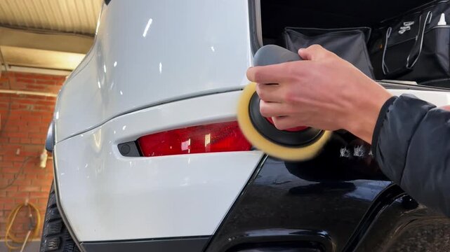 A car service worker polishes the car body with a polishing machine. Detailing and polishing of the car. Car detailing - hands with an orbital polishing machine in an auto repair shop.