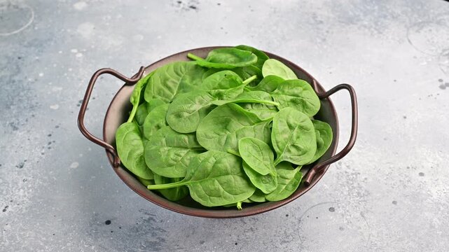 Fresh spinach leaves in a metal bowl on a gray countertop at a kitchen