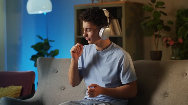 Positive teen boy listening to music in headset and playing invisible drums