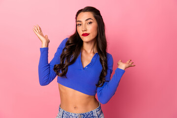 Young chic woman in blue cropped top poses with playful gestures against pink background for...