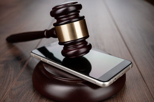Wooden gavel on smartphone placed on round base. Concepts of court case in technology space and regulation.