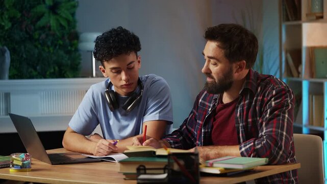 Caring father helping his teenage son with homework, explaining task on laptop