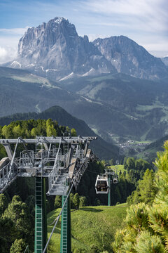 View of a cable car lift ascending over green alpine meadows with the massive Sassolungo mountain peak in the background South Tyrol, Trentino-South Tyrol, Italy.
