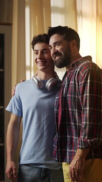 Happy father embracing his teenage son at home, feeling proud of his child