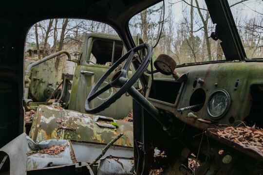 View of the rusted interior of an abandoned truck with a steering wheel and moss-covered dashboard in a forest Pryp'yat', Kyiv Oblast, Ukraine.