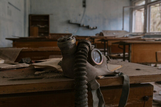 View of an old gas mask on a wooden desk in an abandoned classroom with peeling walls and scattered books in Prypyat, Kyiv Oblast, Ukraine.