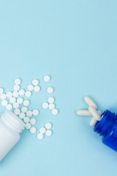 Top view of two jars with scattered pills on a light blue background. Pharmaceutical treatment, medication management, and health concept with copy space for design or advertising