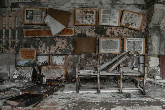 View of an abandoned room with decaying walls, Soviet-era posters, and broken wooden benches in Prypyat, Kyiv Oblast, Ukraine.