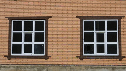 Fototapeta premium Two large windows with plastic frames and crossbars and broken glass from a thrown stone in the structure of a light brick house, the concept of danger and crime in residential areas